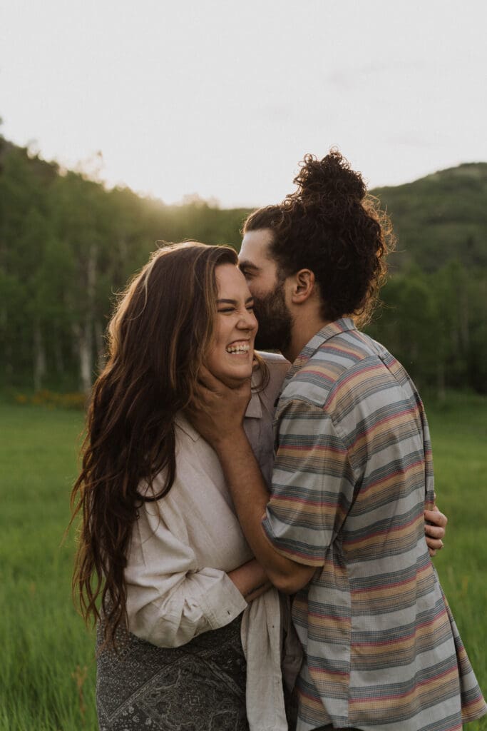 Couple laughing together on a trail surrounded by yellow wildflowers and tall green grass
