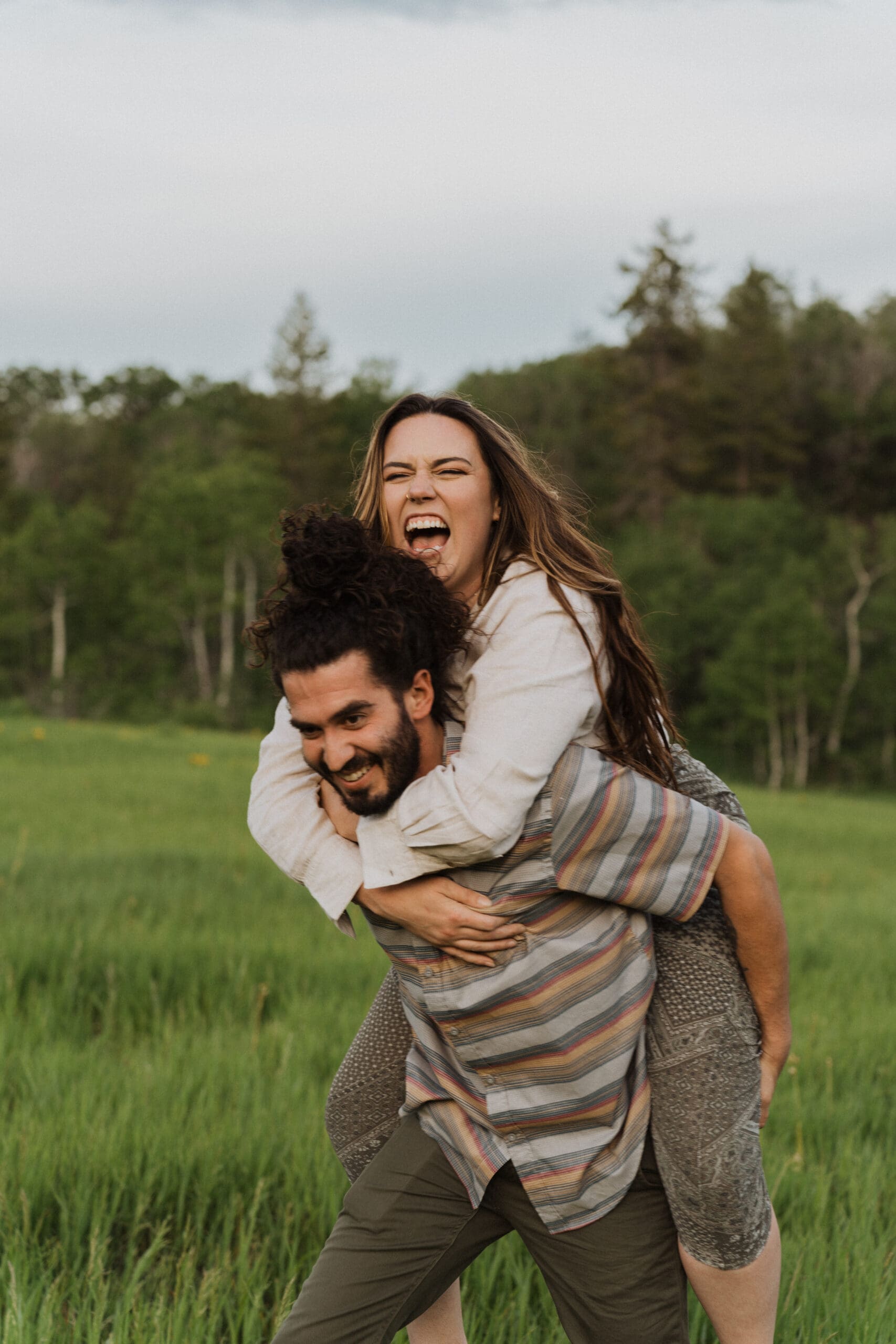 Couple laughing together on a trail surrounded by yellow wildflowers and tall green grass