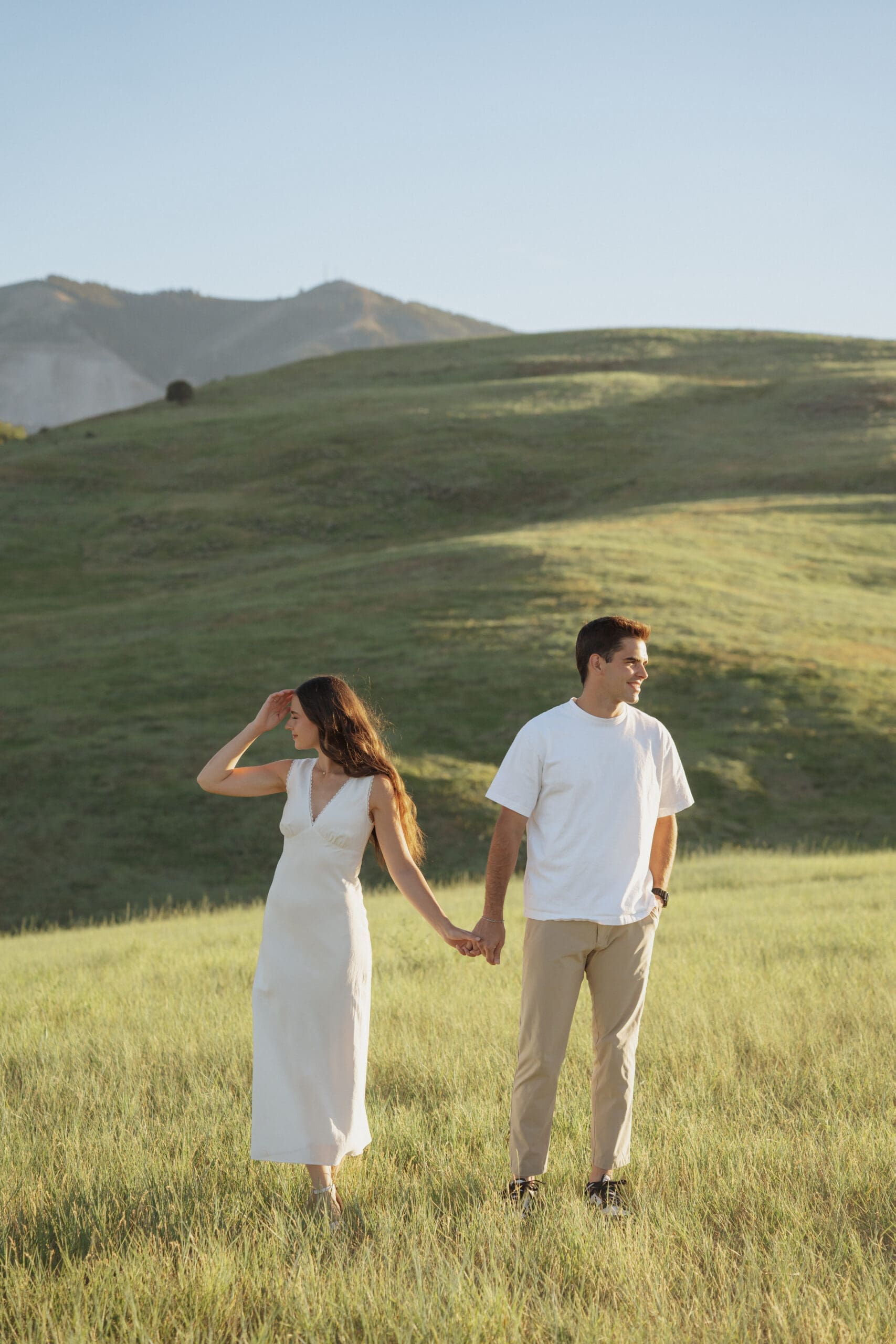 Couple embracing during Wellsville engagement photos in a green hillside field
