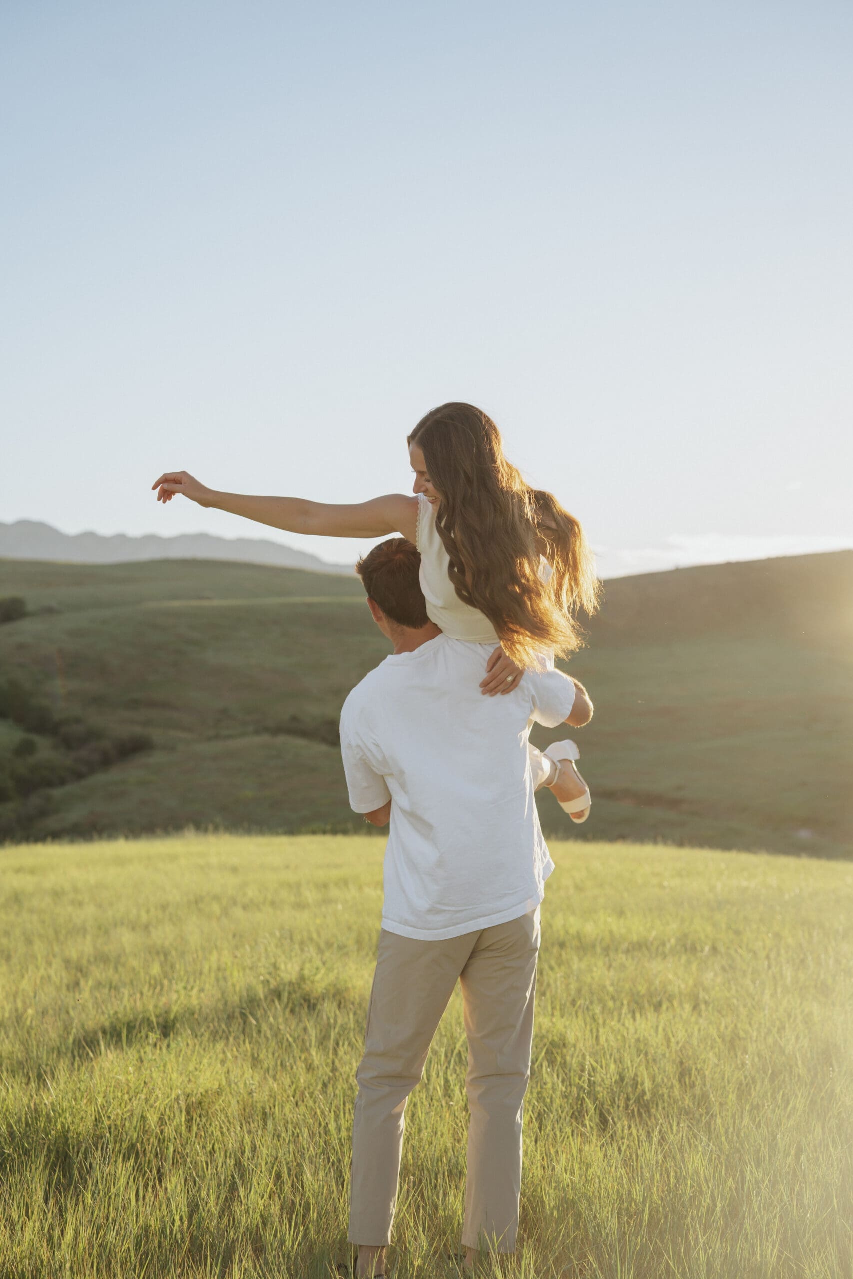 Couple dancing and laughing in a golden-lit meadow with mountains in the background