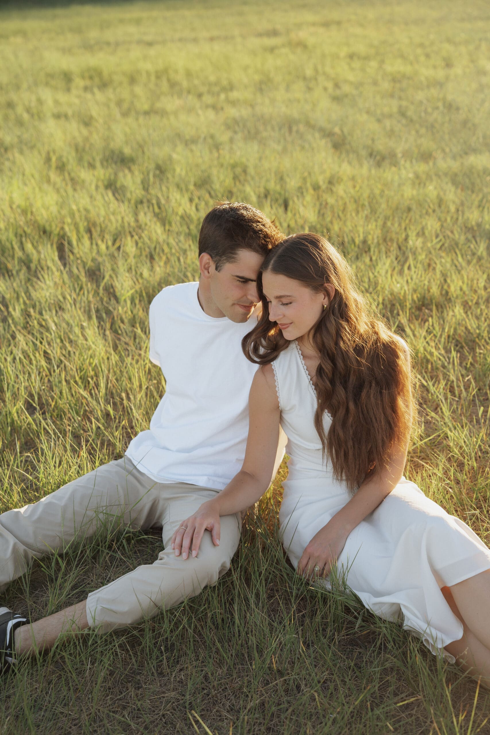 Man kissing woman's cheek while she laughs, arms raised, in a grassy field with rolling hills