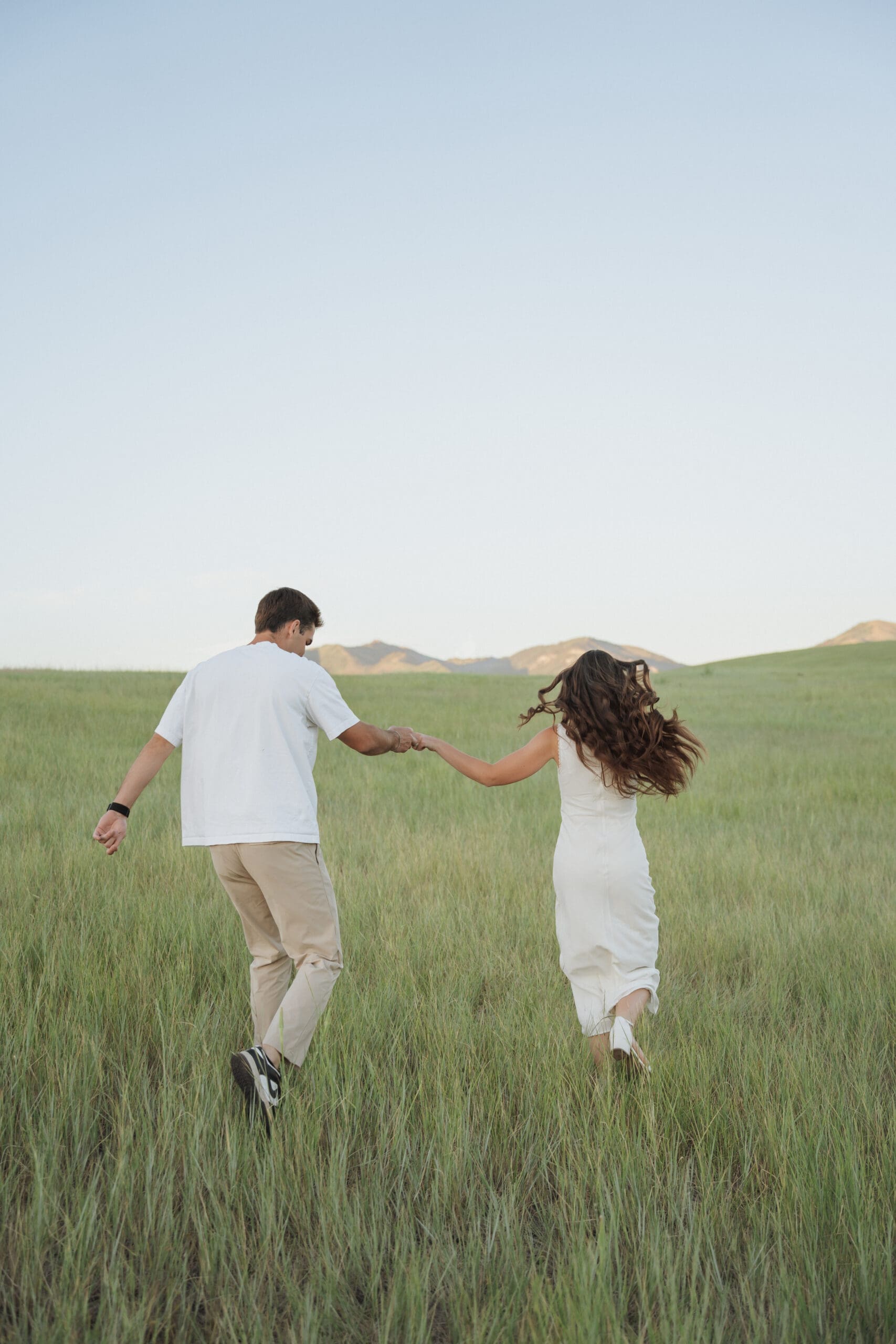 Couple dancing and running in a golden-lit meadow with mountains in the background and blue sky