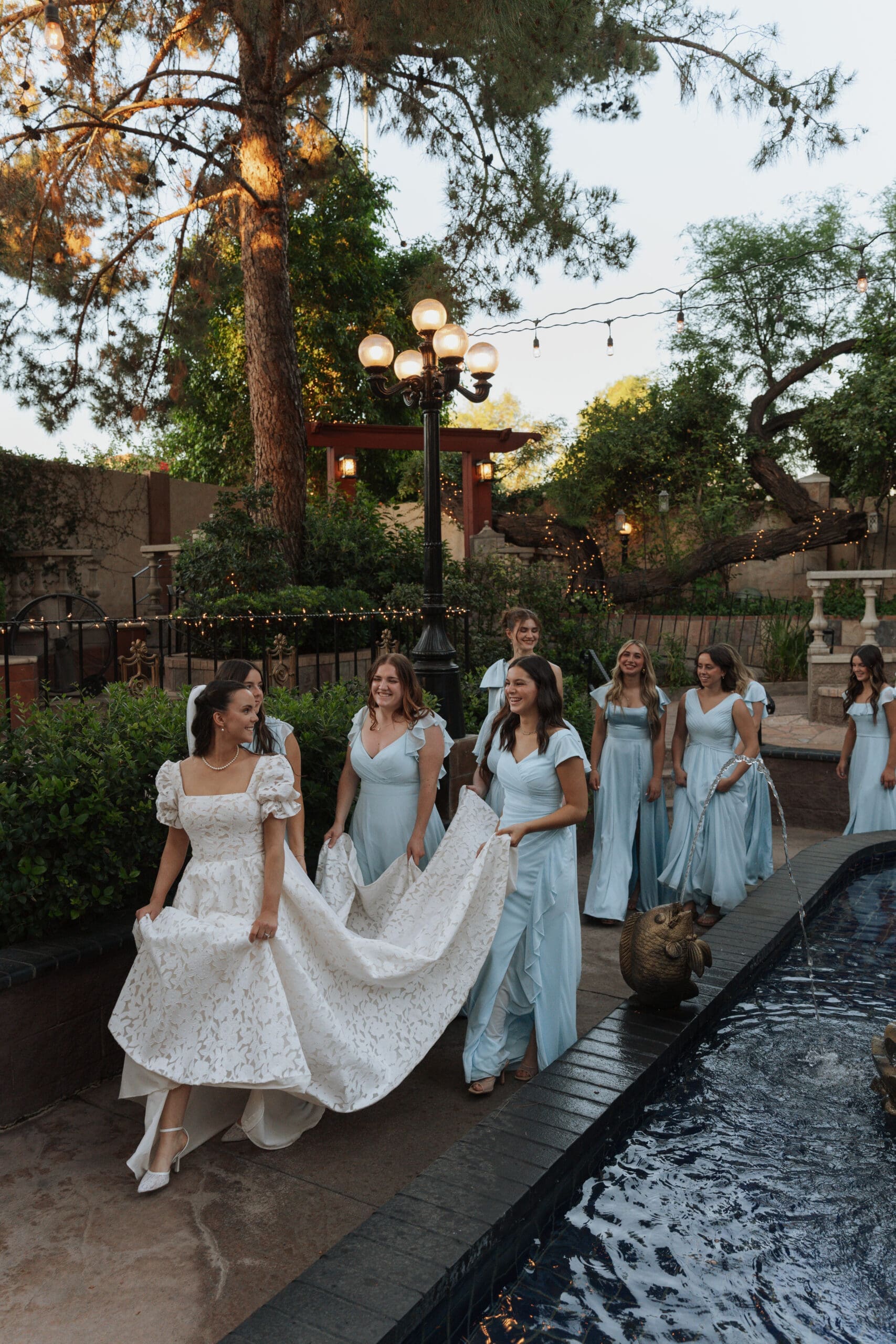 bridesmaids holding the brides dress walking around a fountain